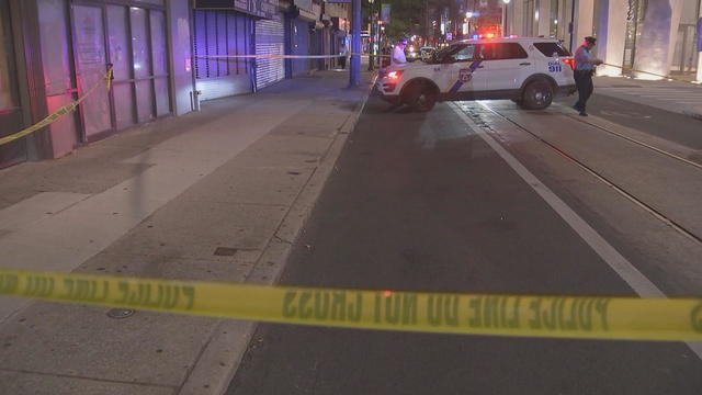 Police tape and a police car are seen near a crime scene in Philadelphia; an officer is standing outside of the car 