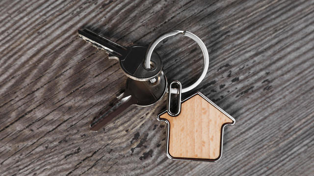 Keys with trinket in shape of house on wooden table, top view. Real estate agent services 