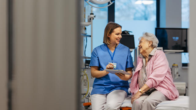 Portrait of caring nurse and senior patient talking in hospital examination room. Emotional support for elderly woman. 