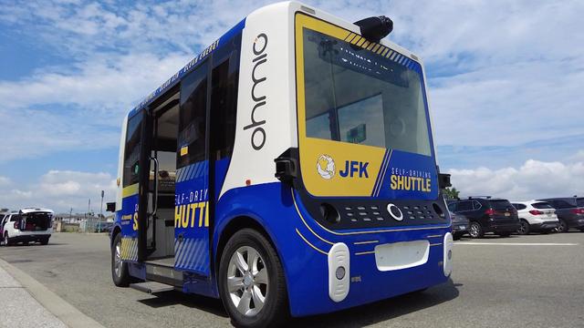 A cube-shaped self-driving shuttle vehicle in a JFK Airport parking lot. 