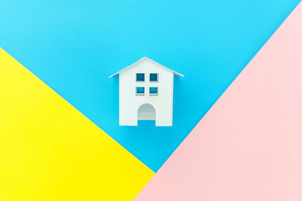 Simply design with miniature white toy house isolated on blue yellow pink pastel colorful trendy geometric background Mortgage property insurance dream home concept. Flat lay top view copy space 