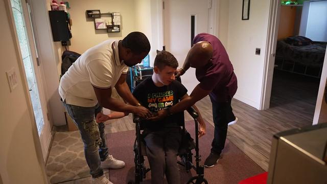 Two aides help strap Chase Sadowski into his wheelchair. 