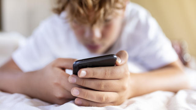 teenager boy is using smartphone at home in bed 