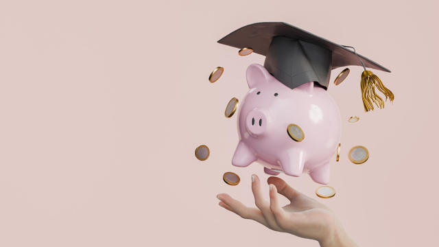 Pink Piggy Bank with Graduation Cap and Coins in Hand on Pink Background 