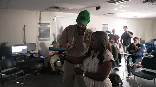 An NYPD official shows CBS New York's Jennifer Bisram how to handle a fake firearm during a simulator training. 