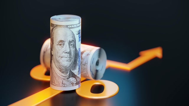 Rolled Up 100 American Dollar Bills Sitting Over Orange Colored Arrow Symbol On Black Background 