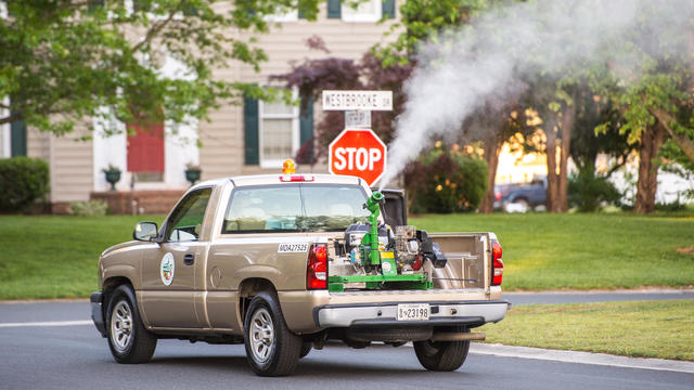 Mosquito Control Truck drives through suburban neighborhood spraying insecticide to control mosquito population 