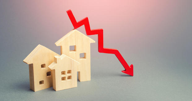 Miniature wooden houses and a red arrow down. The concept of low cost real estate. Lower mortgage interest rates. Falling prices for rental housing and apartments. Reducing demand for home buying 