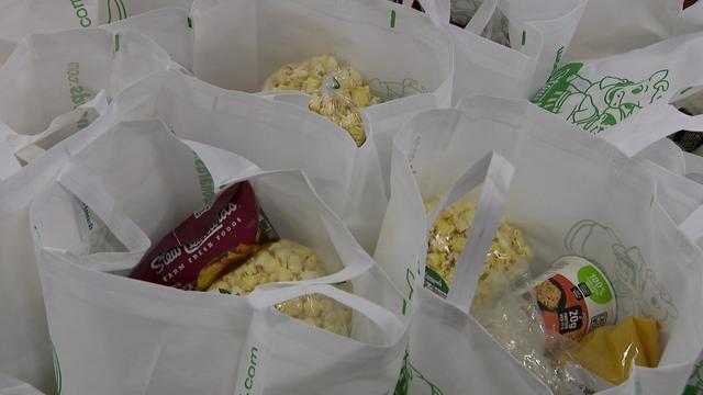 Several reusable Stew Leonard's groceries bags sit on the floor with food items inside. 