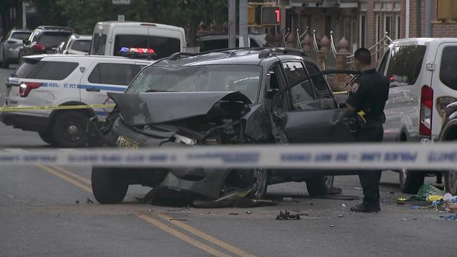 A minivan with severe damage to its front end and roof behind crime scene tape on a Brooklyn street. 