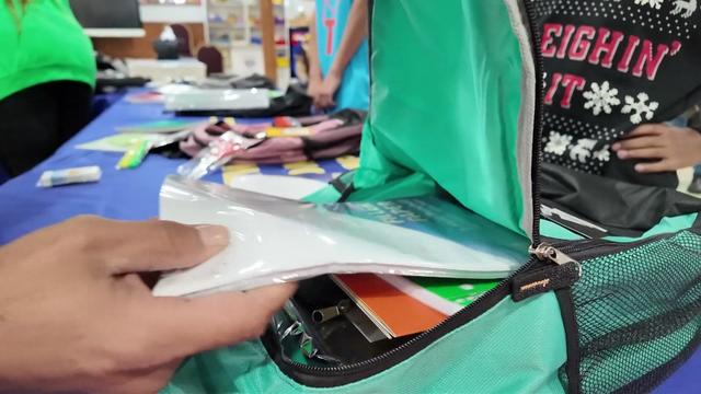 An individual puts supplies into a child's backpack. 