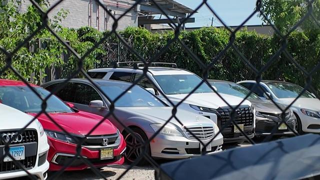 Several vehicles parked in a lot behind a chain-link fence. 