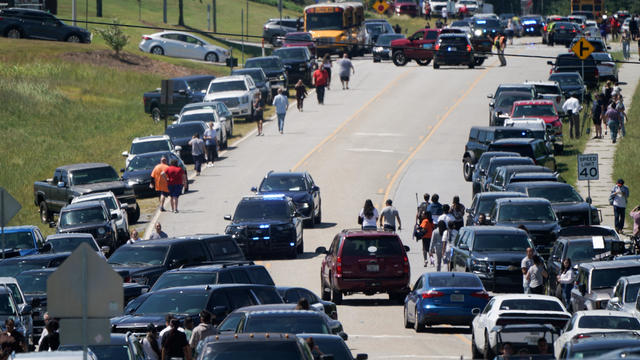 People walk by cars parked on the side of a road near the scene of a shooting at Apalachee High School in Winder, Georgia, Sept. 4, 2024. 