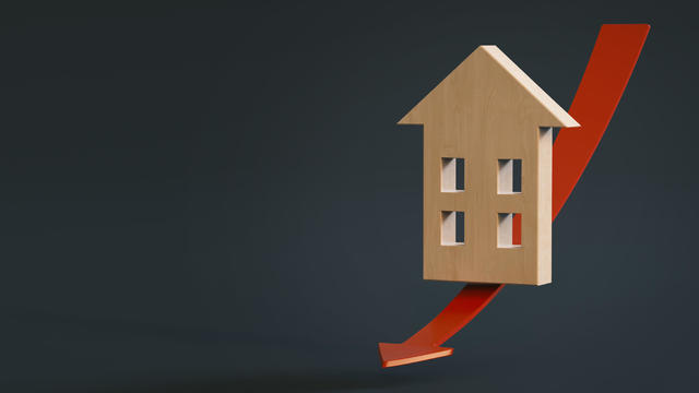 Stylized mockup of a wooden house slides down a red arrow pointing down on a dark background with space for text or logo. 3D rendering. Falling property prices 