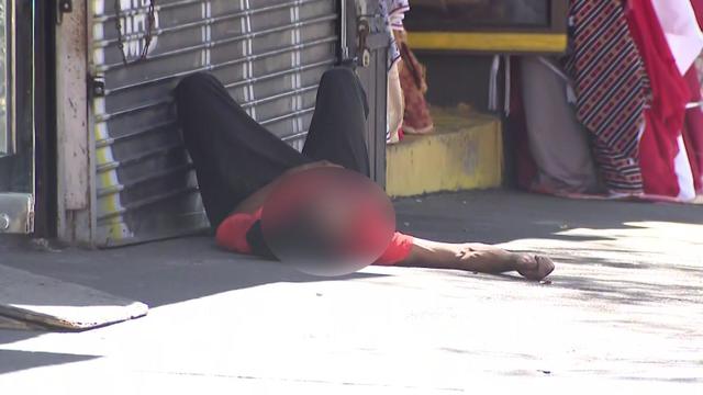 A man lays on the sidewalk outside a storefront in the Bronx. 