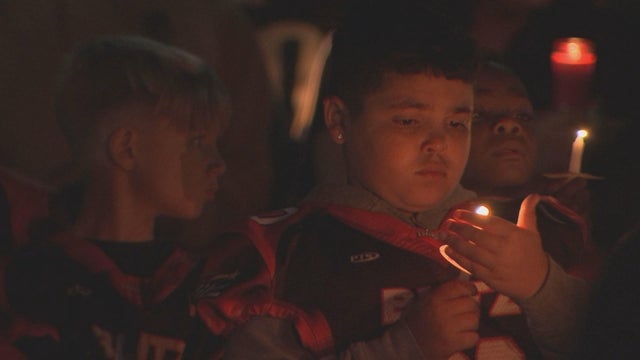 A child holds a hand near a candle during a vigil for the coach