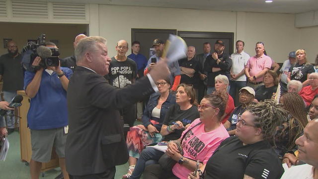 A union representative gestures with a stack of paper while speaking to the crowd at a meeting 