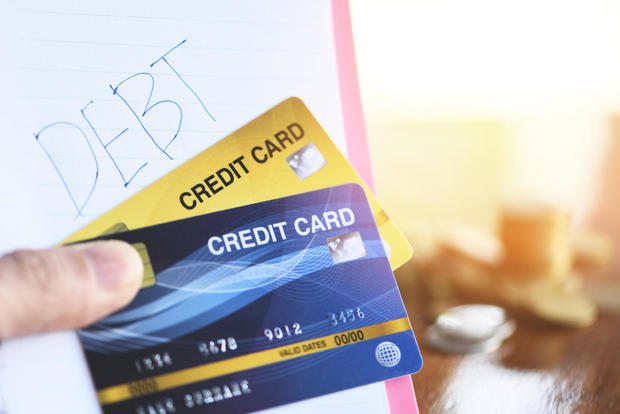 Debt credit card in hand and coin stack on the wooden table at the office background - debt management concept 