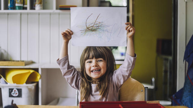 Portrait of happy girl showing color pencil scribble on paper at kindergarten 