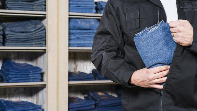 Shoplifter stealing denim jeans in his jacket 