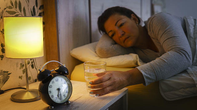 Woman in bed reaching glass of water early morning 