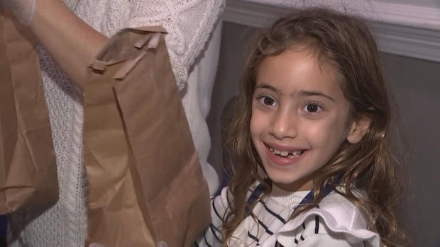 A smiling girl holds a brown paper bag containing ingredients to make challah 