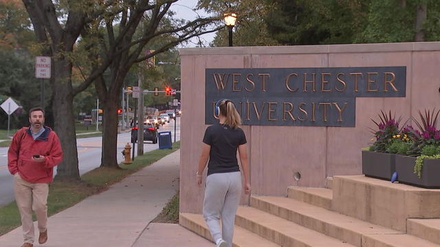 People walk near a sign for West Chester University 