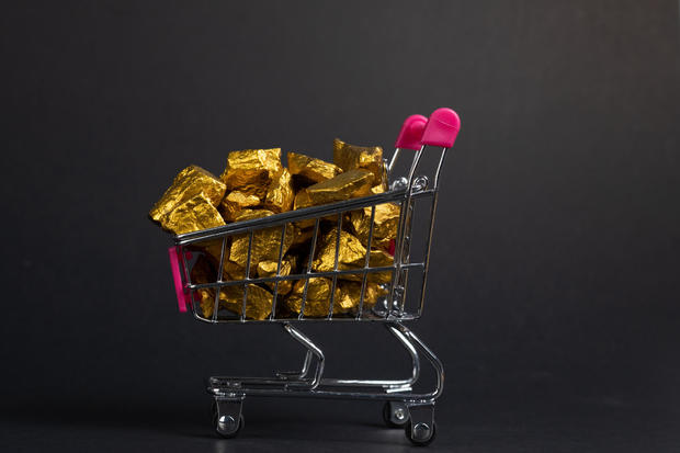 A pile of gold nuggets or gold ore in shopping cart or supermarket trolley on black background, precious stone or lump of golden stone, financial and business concept. 