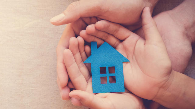 Adult and child hands holding blue paper house for family home and homeless shelter concept 