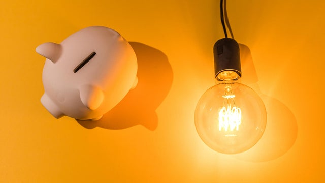 Piggy bank next to lit light bulb on pink background. Concept of electricity price, crisis, money, saving and power energy. 