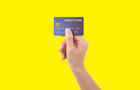 Female hand holding blue credit card on yellow background 