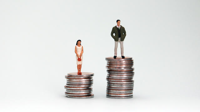 A miniature man and woman standing on a pile of coins at different heights. 