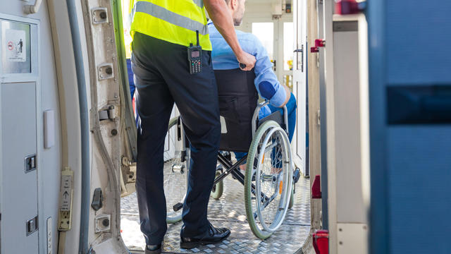 Service man helping disabled passenger to enter on board at airport 