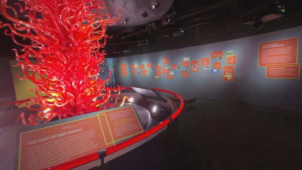 A large piece of glass artwork that resembles a fire is seen in the museum 