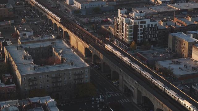 An aerial view of subways traveling along elevated tracks in a New York City neighborhood. 