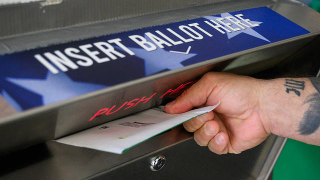 A hand drops a ballot into a box that says Insert Ballot Here 