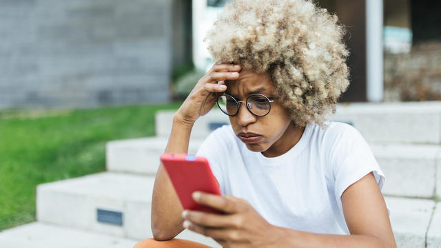 Afro woman looking worried and stress while reading bad news on her mobile phone. 