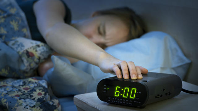 Woman waking up early with alarm clock 