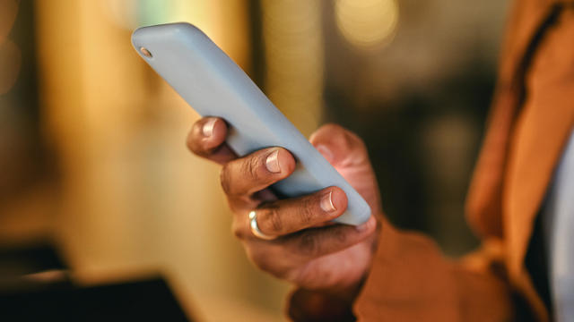 Close up of hands of teen boy in white sweater texting on phone. 