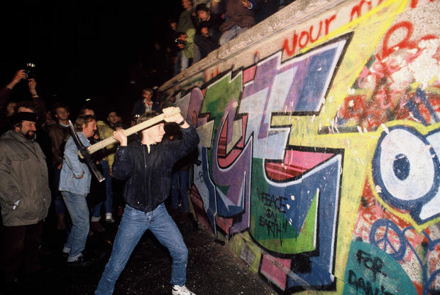 A man attacks the Berlin Wall with a pickaxe on the night of November 9th, 1989 