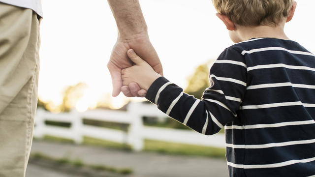 Rear view of father and son holding hands while standing outdoors 