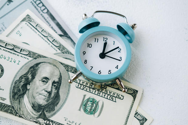 Alarm clock lying on one-hundred-dollar bills. 