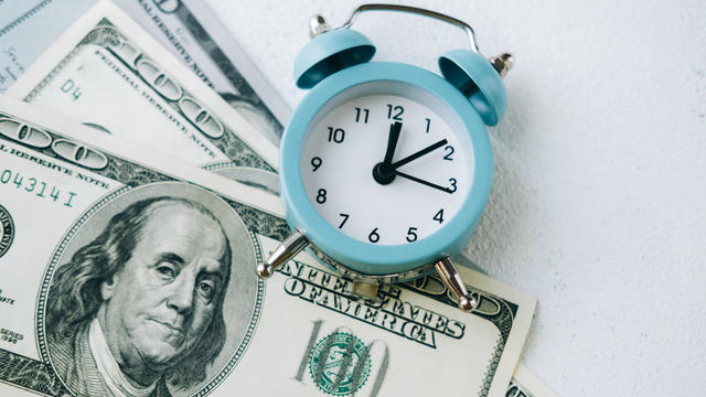 Alarm clock lying on one-hundred-dollar bills. 