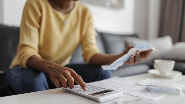 Close up of a mid adult woman checking her energy bills at home, sitting in her living room. She has a worried expression 