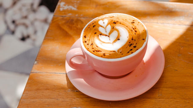 Cappuccino in a pink cup with a beautiful latte art on a wooden table. Cappuccino with nut milk 