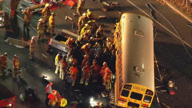 Overhead view as emergency crews surround a pickup truck that is wedged under a bus, trying to extricate the driver 