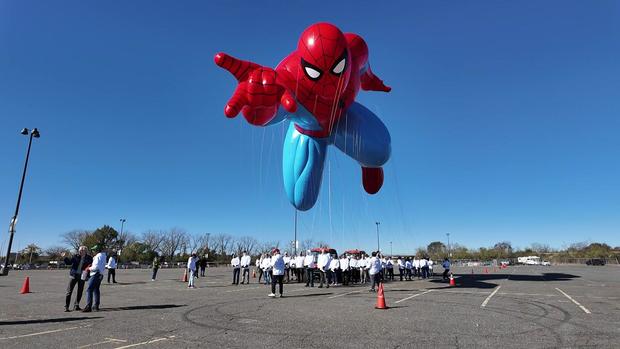 A balloon of Spider-Man floats above dozens of balloon handlers in a parking lot. 