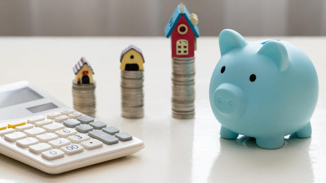 Mini house on stack of coins. Piggy bank and stacked coins on white wooden table. Property investment and house mortgage financial concept 