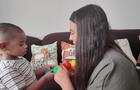 A 2-year-old child looks at a toy held by his speech therapist. 