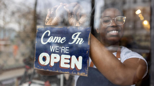 African woman hanging an open sign on the glass door of zero waste grocery store 